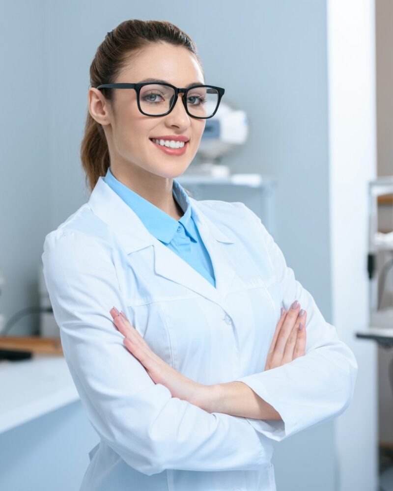 attractive professional ophthalmologist in glasses standing with crossed arms in optical clinic